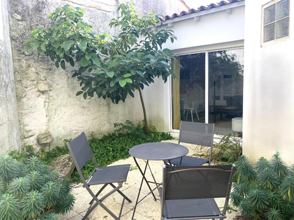 a table and chairs in a courtyard with a tree at Petite maison de village Eloise proche de la plage in Sainte-Marie-de-Ré