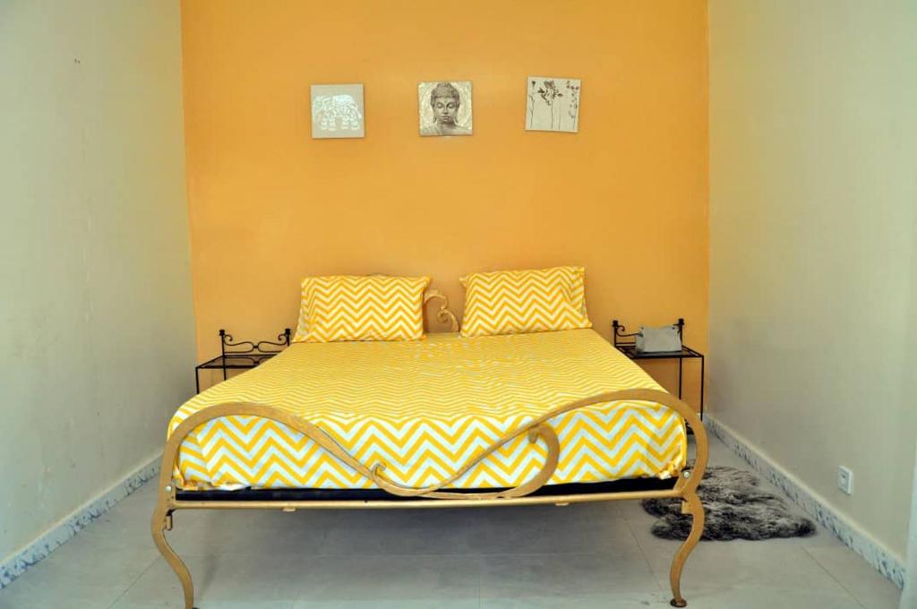 a bedroom with a bed with a yellow wall at Kër Fina in Saly Niakh-Niakhal