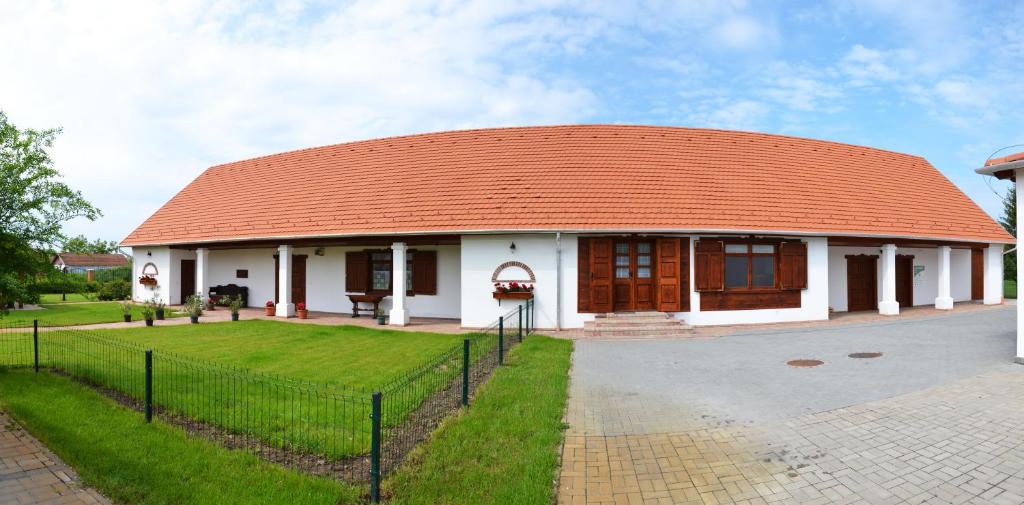 un edificio con techo rojo y patio de césped en Falusi Patika - Tisza-tó Vendégház, en Tiszaszőlős