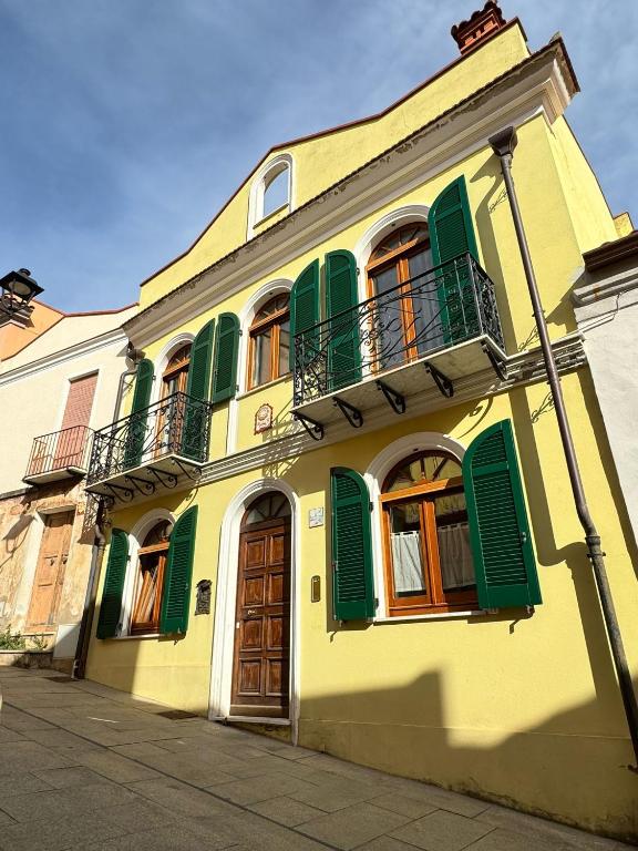 a yellow building with green shutters and a balcony at Casa Antonietta - SHARDANAPARTMENTS in Iglesias