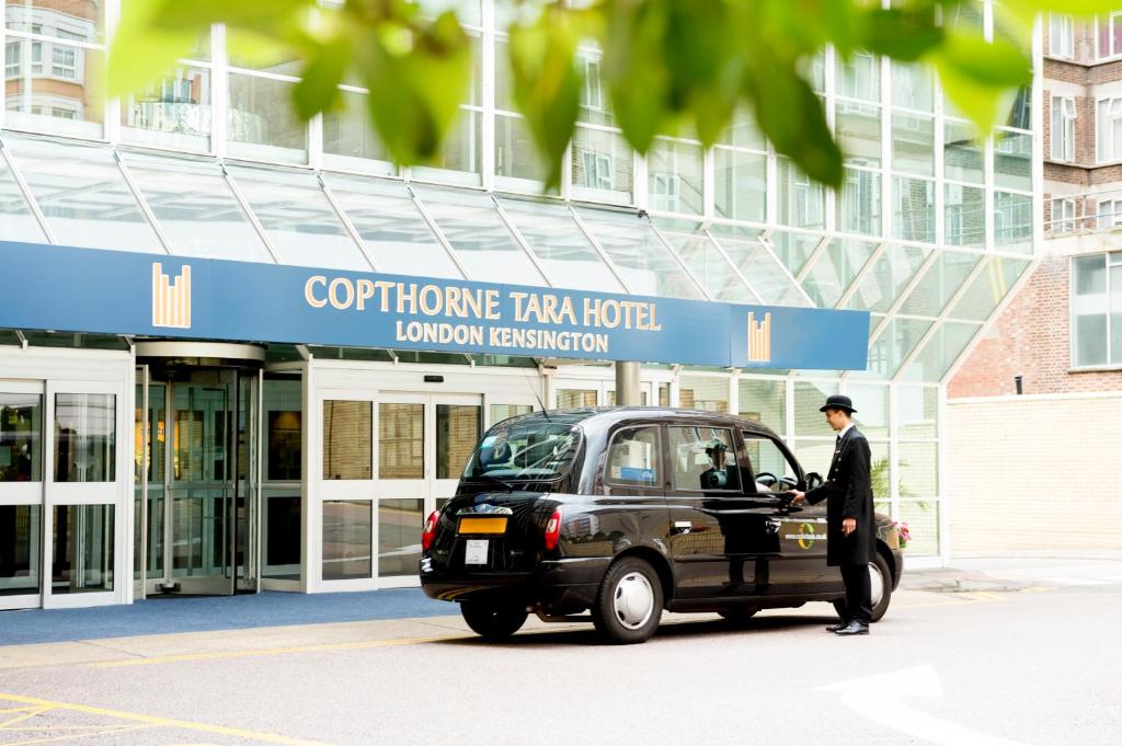 two men are driving a car in front of a building at Copthorne Tara Hotel London Kensington in London