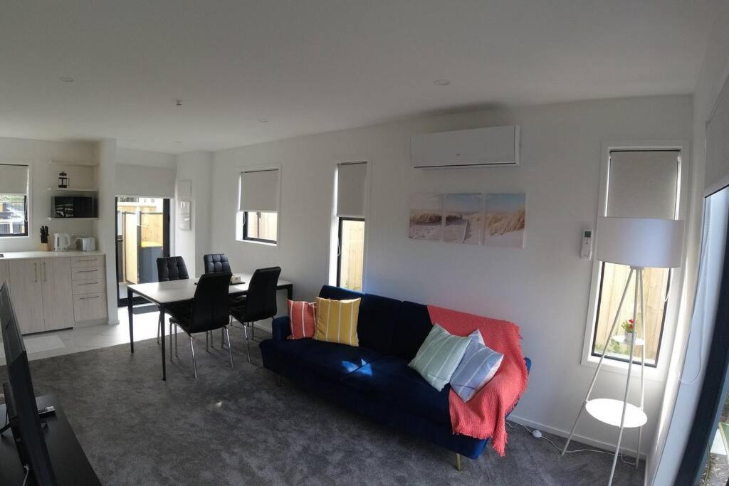 Una sala de estar con un sofá y una mesa con sillas. en C-Side-R, Modern Beachfront Living, en Christchurch