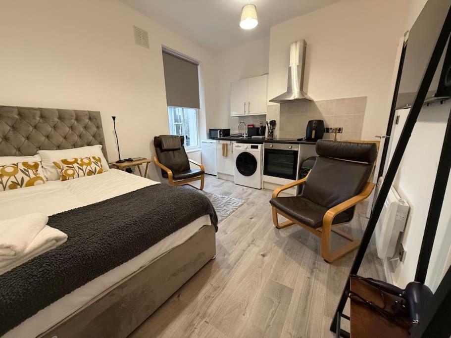 a bedroom with a bed and two chairs and a kitchen at Cosy Studio Central Colwyn Bay F2 in Colwyn Bay