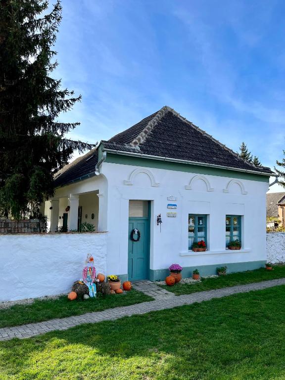 a woman sitting in front of a white house at Öregfenyő Tornácosház in Bakonykoppány