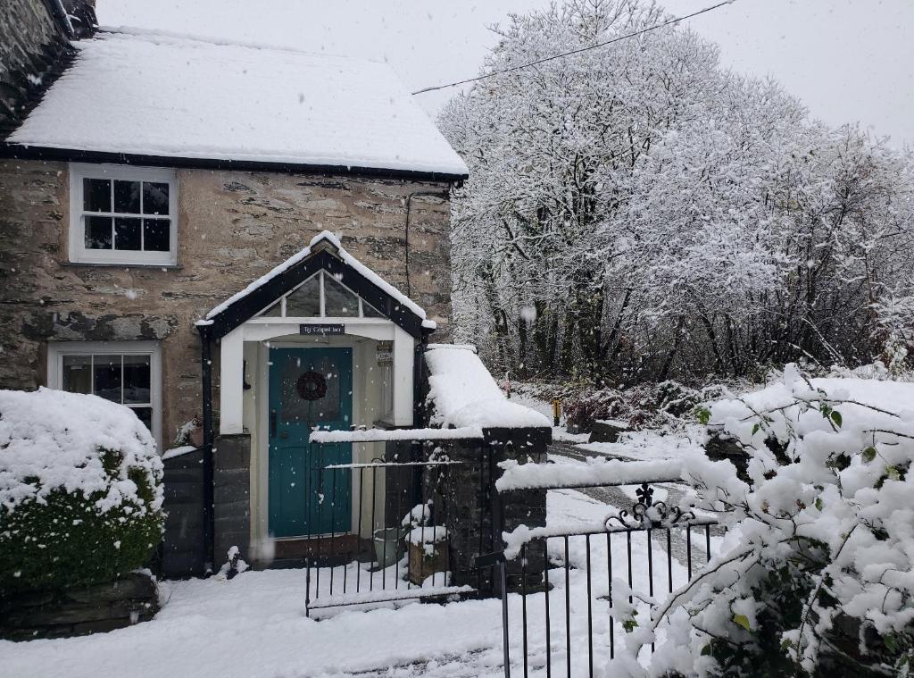 een stenen huis met een groene deur in de sneeuw bij Ty Capel Isa in Blaenau-Ffestiniog