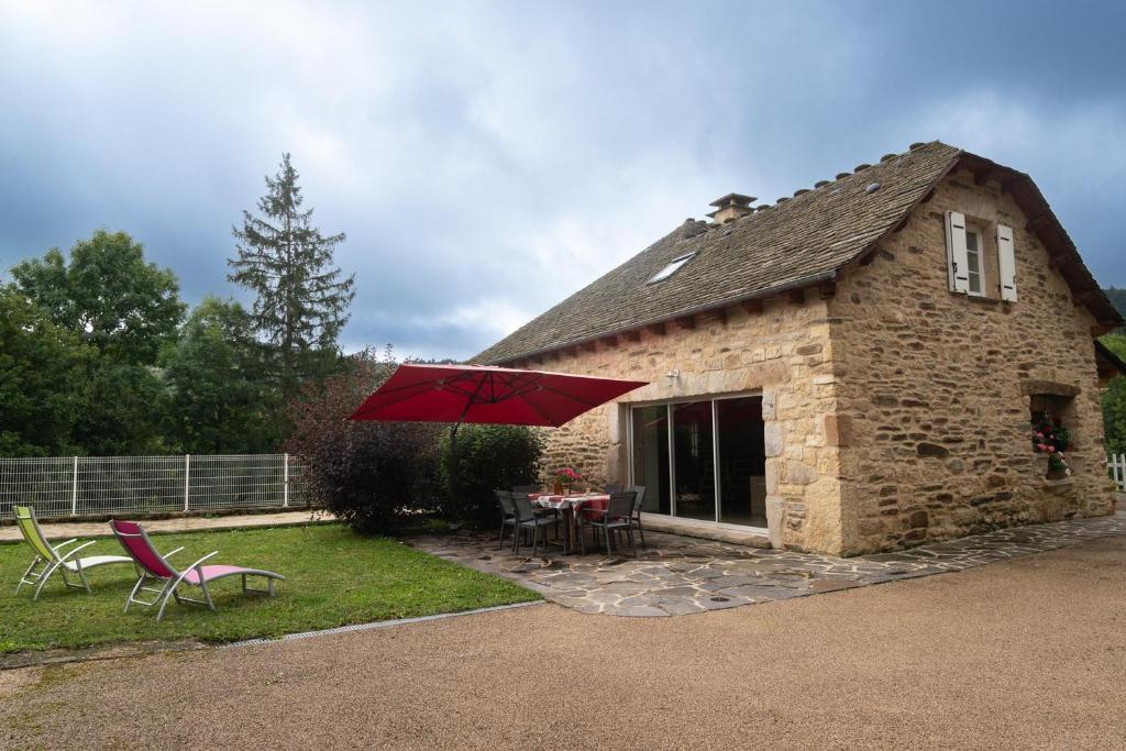 a stone house with a table and chairs and a red umbrella at Gîte a les rosiers in Chadenet