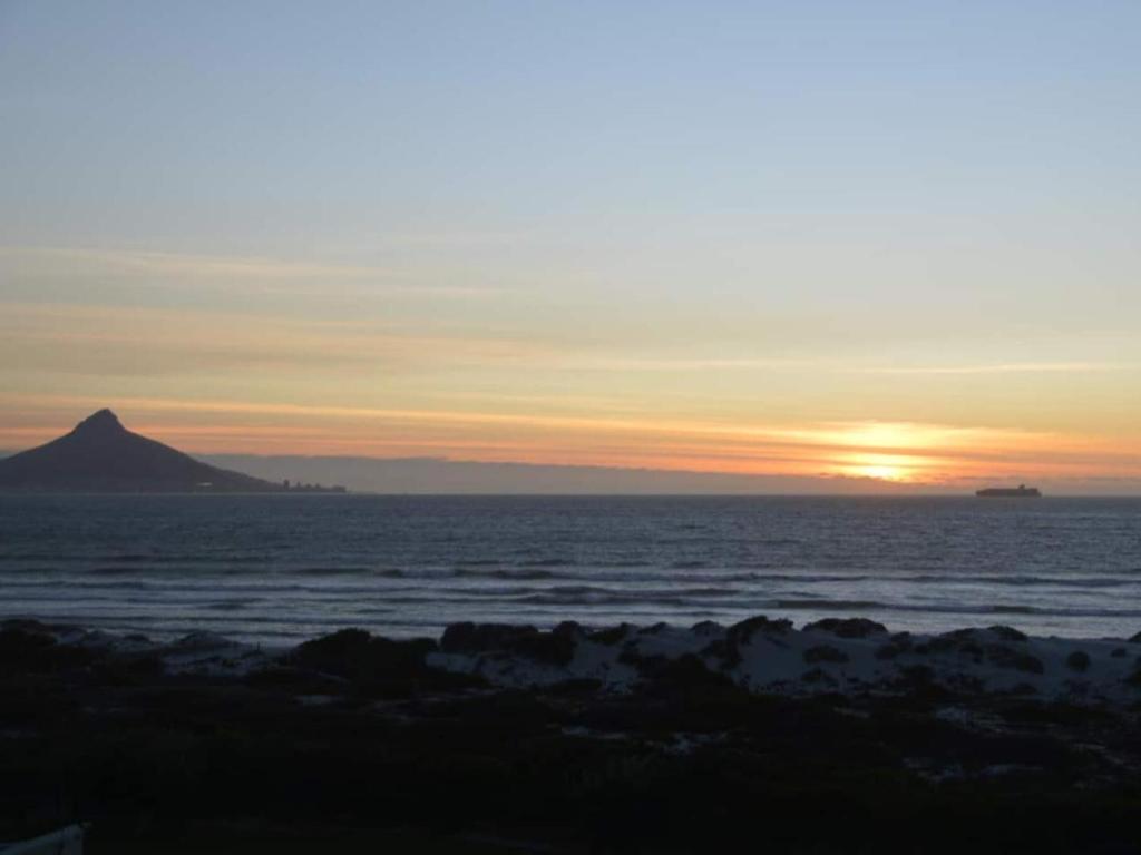 un coucher de soleil sur l'océan avec une montagne au loin dans l'établissement Dolphin Delight, à Bloubergstrand