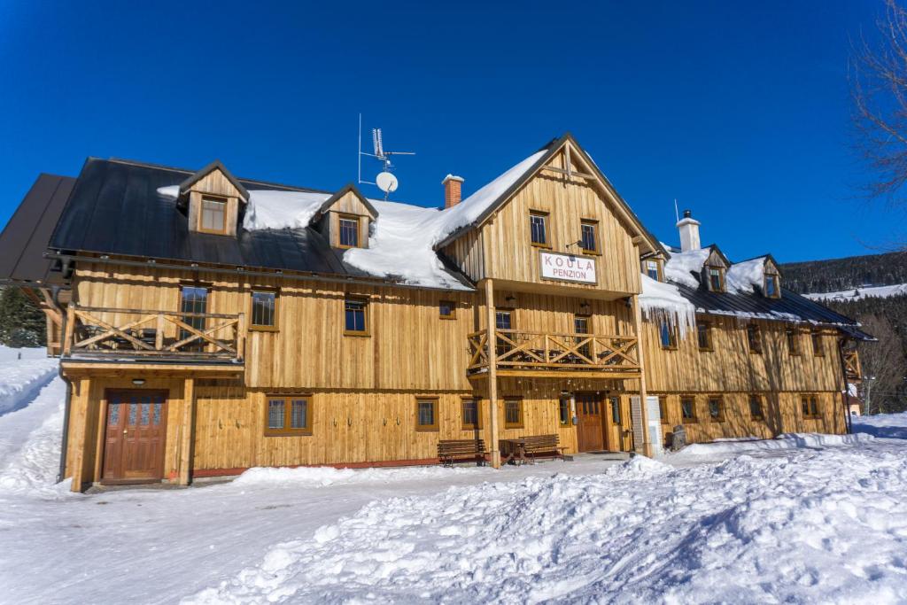 a large wooden building with snow on it at Koula Apartments in Pec pod Sněžkou