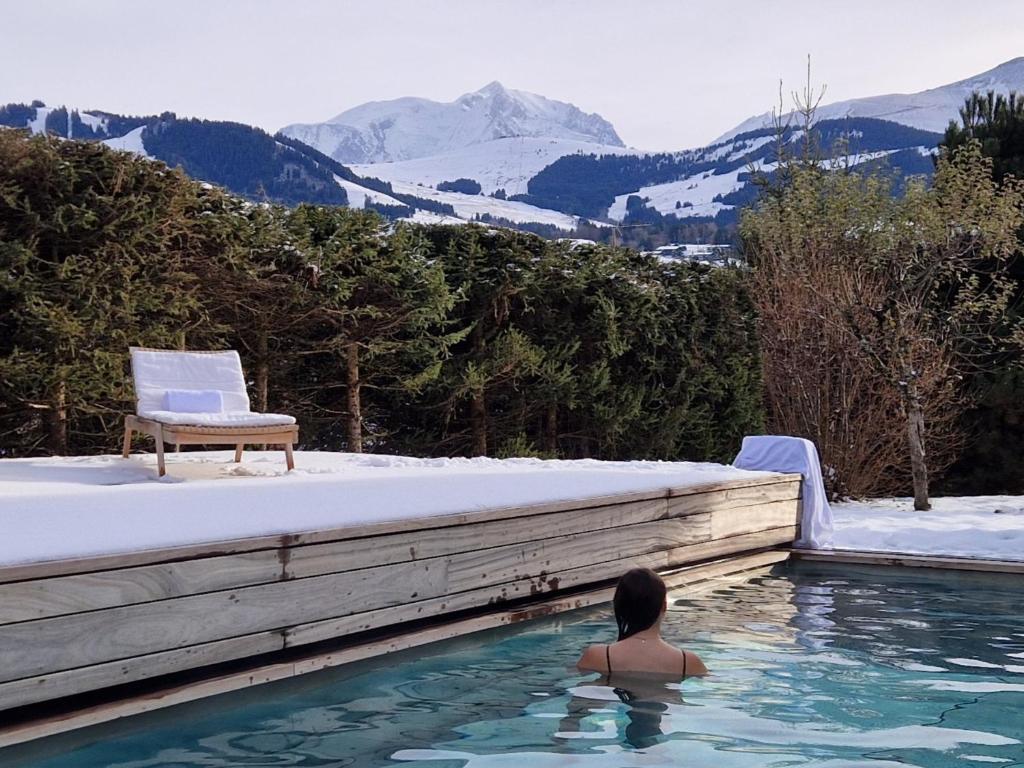 a person in a swimming pool with a chair and mountains at L'Alpaga, a Beaumier hotel in Megève