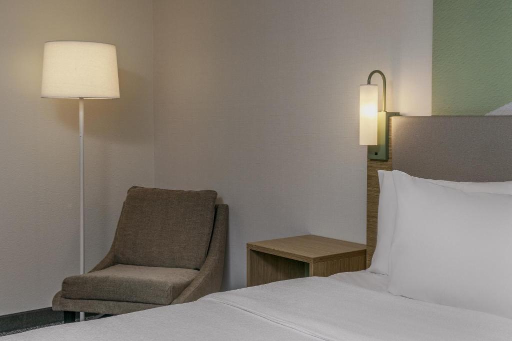 a bedroom with a bed and a chair and a lamp at Spark by Hilton Denver International Airport in Denver