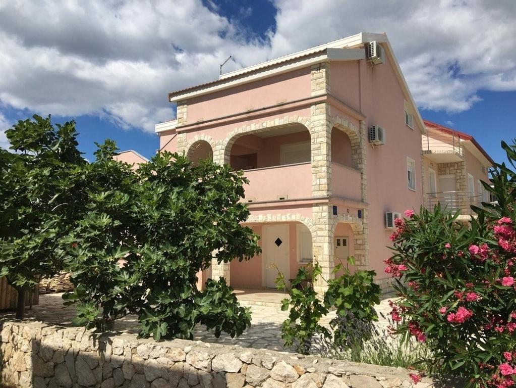 une maison rose avec un mur en pierre et quelques fleurs dans l'établissement Apartments by the sea Mandre, Pag - 6507, à Kolan