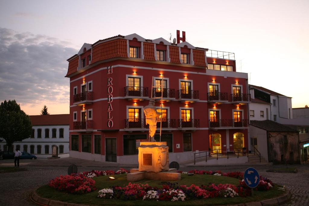 a large red building with a statue in front of it at Hospedaria Robalo in Sabugal