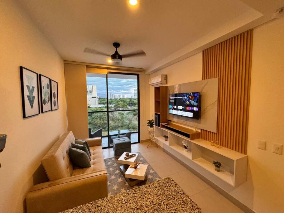 ein Wohnzimmer mit einem TV und einem großen Fenster in der Unterkunft Apartamento Celeste a Pasos del Mar y Aeropuerto in Santa Marta