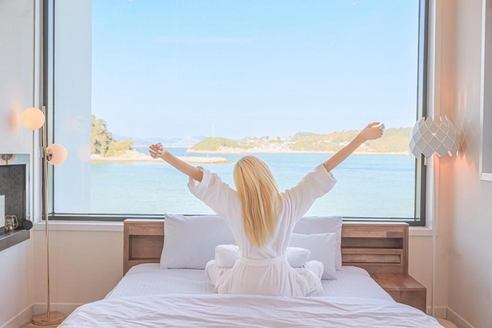 Eine Frau, die auf einem Bett sitzt und aus dem Fenster schaut. in der Unterkunft Geoje Dream Angel Pool Villa in Geoje