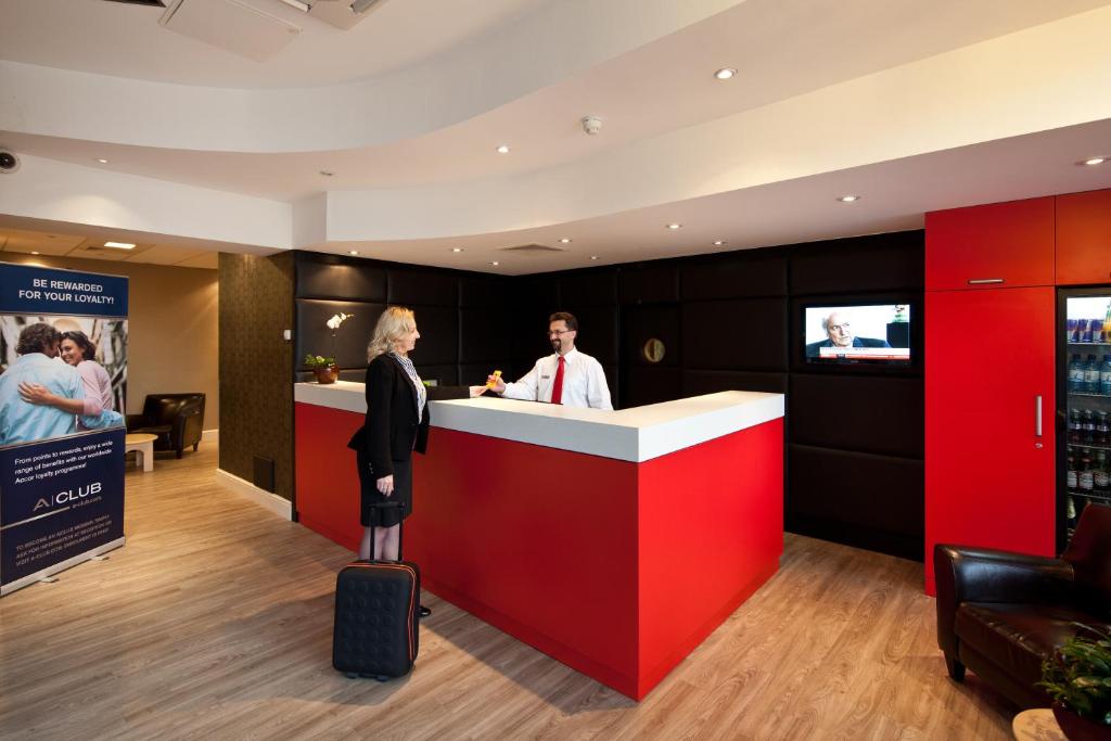 a man and a woman standing at a bar with a suitcase at ibis Stevenage Centre in Stevenage