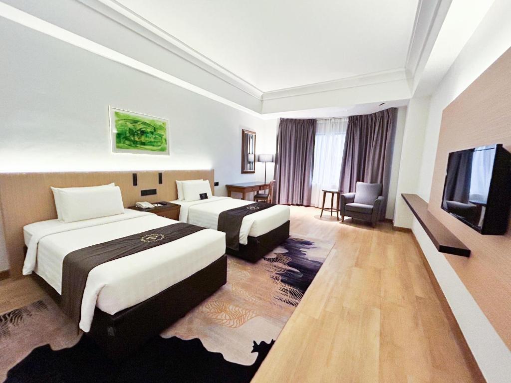 A bright twin room with a wall-mounted television, patterned rug and a lounge corner by the window.