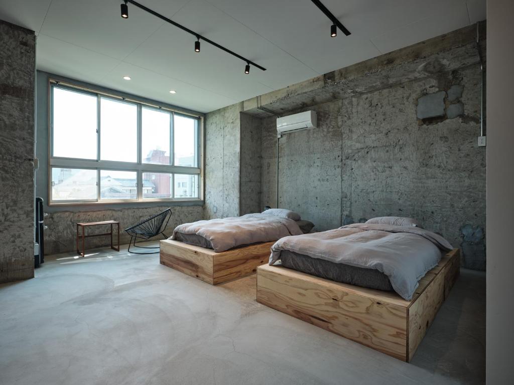 two beds in a room with concrete walls and windows at 三笠館Mikasakan 別館 in Kinokawa
