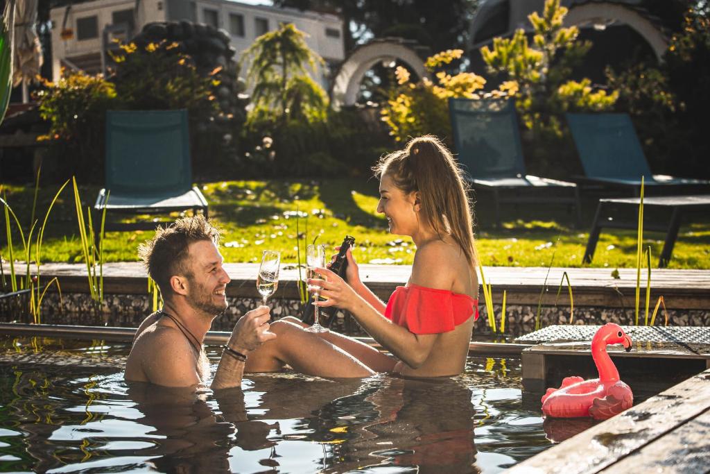 a man and woman drinking wine in a swimming pool at ALPENHOTEL TYROL - B&B - ADULTS ONLY - Alpines Lifestylehotel in Pertisau