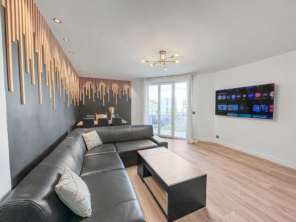 a living room with a black leather couch and a table at Confort moderne, Paris & Le Bourget in Drancy