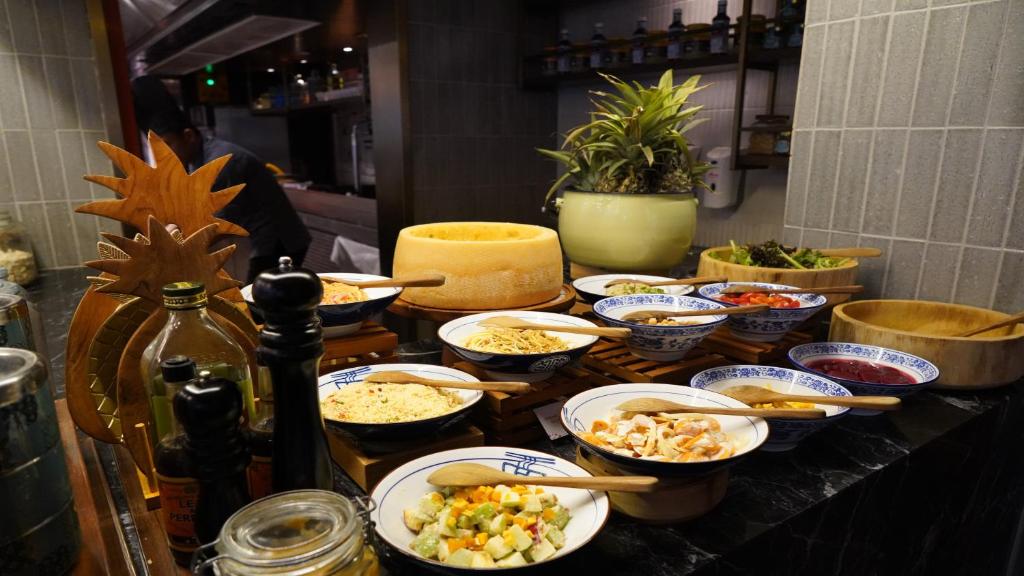 A buffet counter displays bowls of prepared foods, condiments, fruit, and a large cheese wheel.