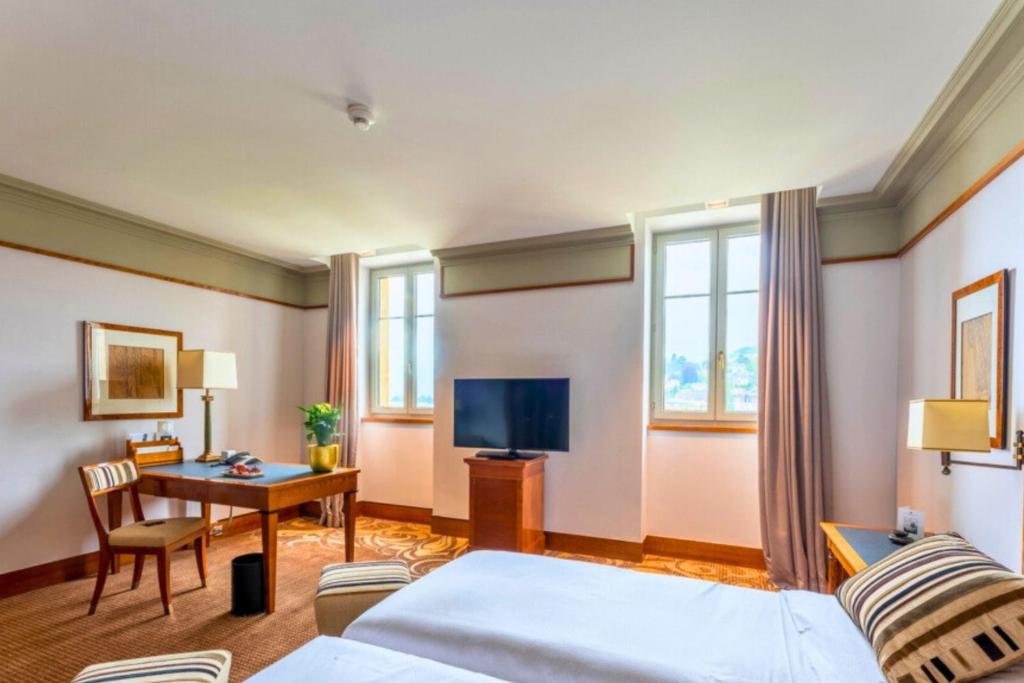 ein Hotelzimmer mit einem Bett, einem Schreibtisch und einem TV in der Unterkunft Beau Rivage Hotel in Neuenburg
