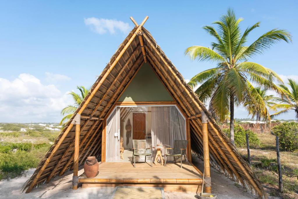 a thatch roofed house with a deck and a palm tree at Cabanas Blue in Mata de Sao Joao
