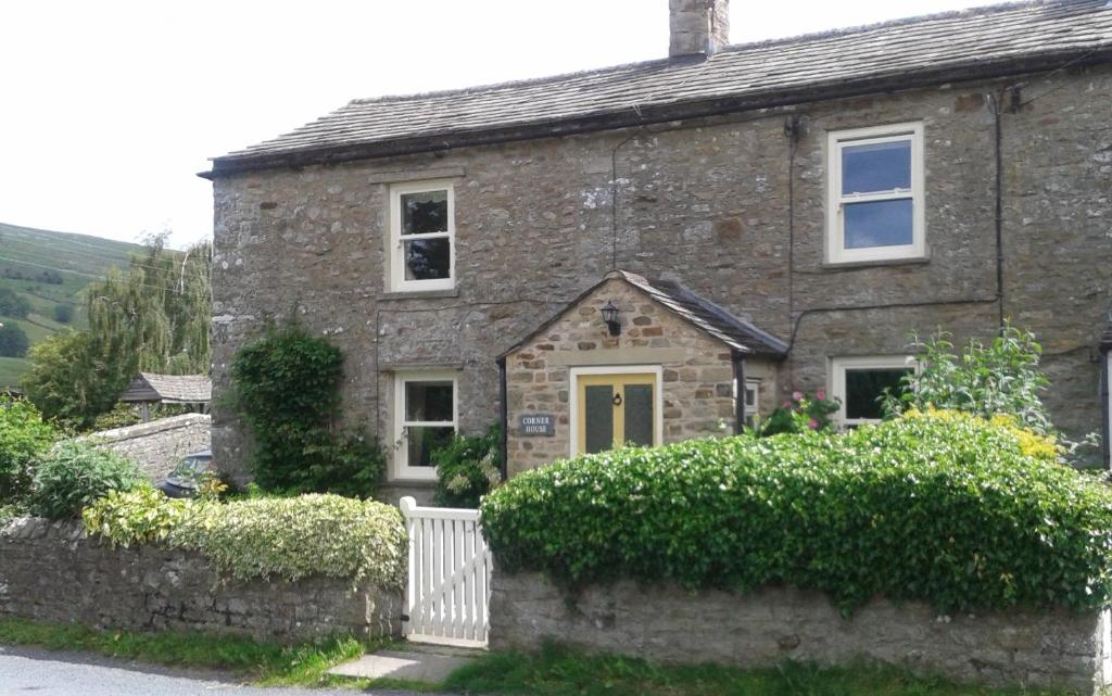 a stone house with a yellow door and bushes at Corner House in Grinton