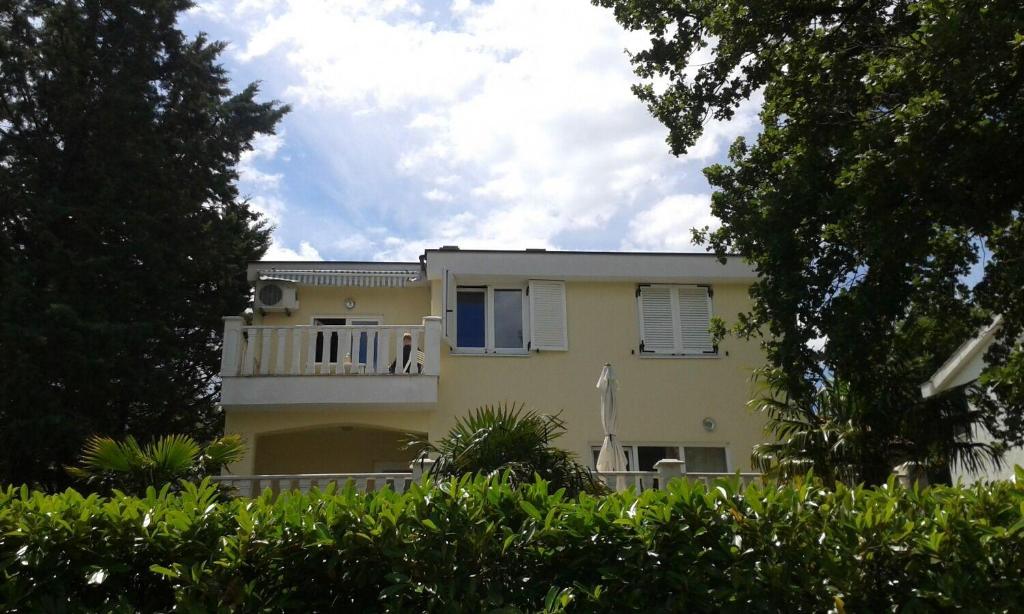 a yellow house with a balcony and trees at Apartments Pondeljak in Malinska
