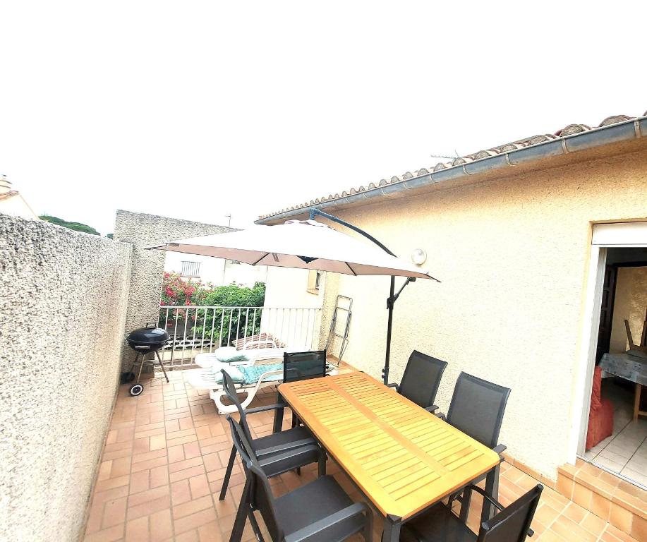 - une table et des chaises en bois avec un parasol sur la terrasse dans l'établissement terrasse privative étage soleil catalan 150m mer 4 pers animaux chéque vacance, à Saint Cyprien Plage