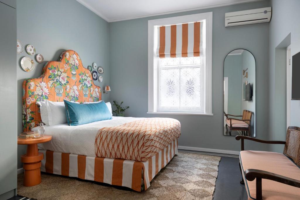 Un dormitorio con una cama, una ventana y un espejo. en Petit Pineapple House, en Ciudad del Cabo