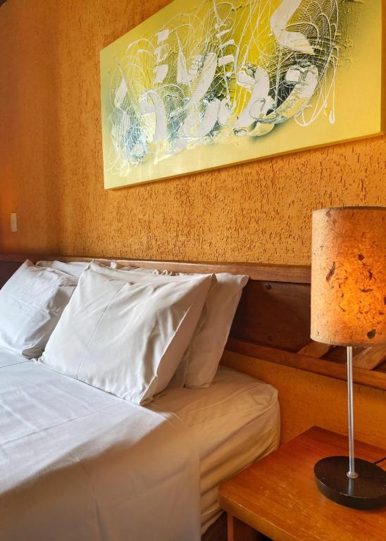 a bed with white sheets and a table with a lamp at Villa Zen Pirenópolis Conforto e Bem-Estar in Pirenópolis