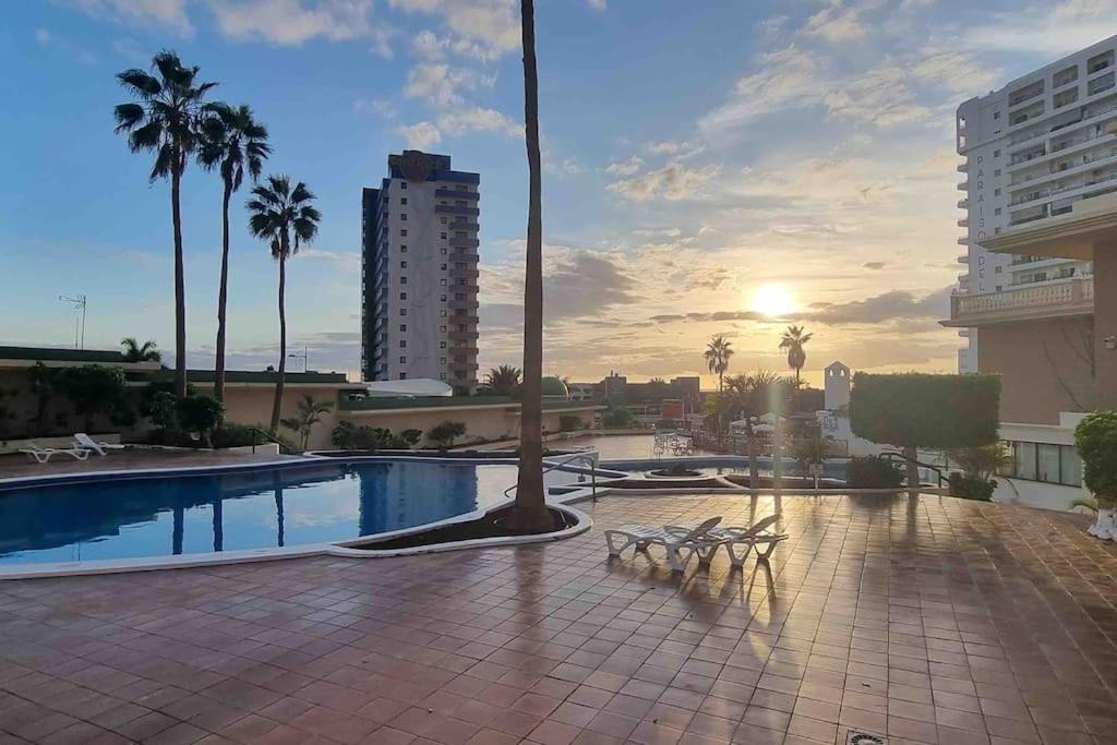 a pool with benches and palm trees and the sunset at Club Paraiso in Adeje