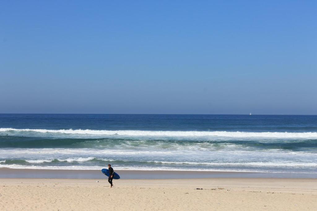 ペニシェにあるPro Touristic Peniche Surf & Beachのサーフボードで海岸を歩く者