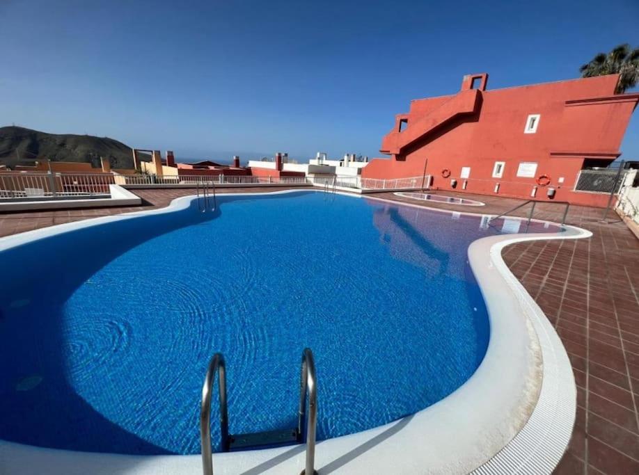 una gran piscina azul junto a un edificio rojo en Ático Mirador del Atlántico, en Chayofa