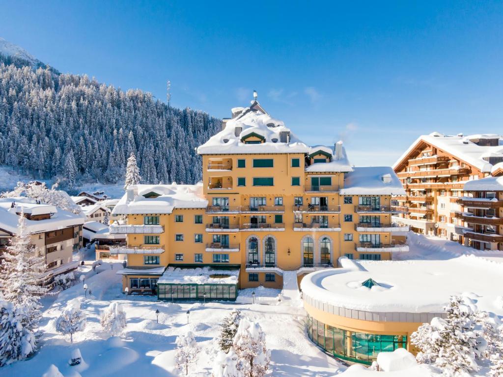 a large yellow building with snow on the ground at Hotel Vereina in Klosters