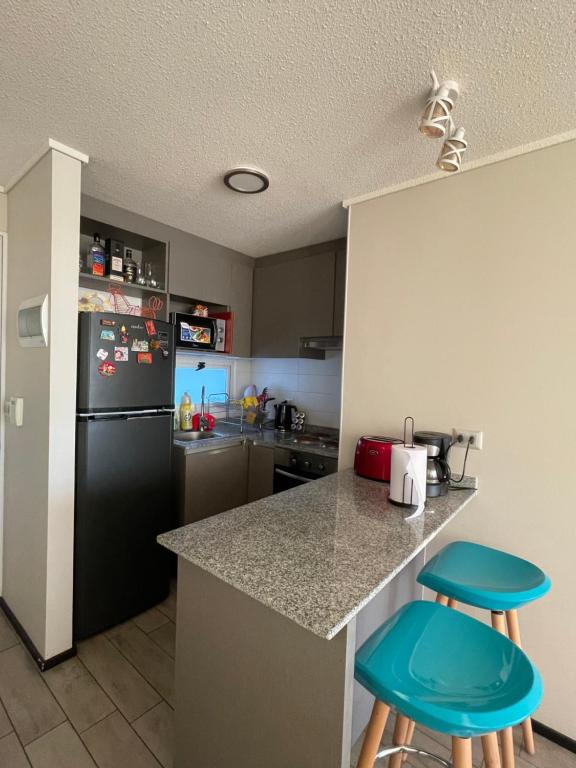 eine Küche mit einem schwarzen Kühlschrank und zwei blauen Hockern in der Unterkunft Departamento cerro barón in Valparaíso