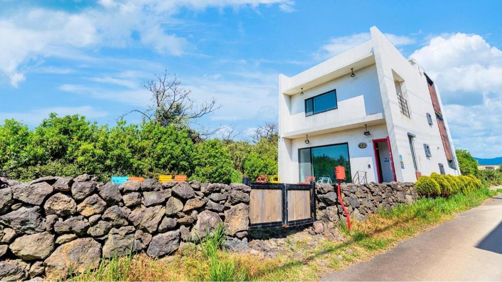une maison blanche derrière un mur en pierre dans l'établissement Jeju Damongchae Pension, à Jeju