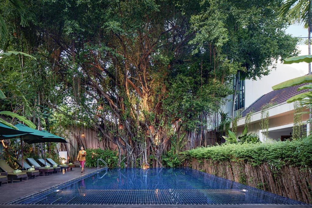 a woman walking by a pool in front of a tree at Lynnaya Urban River Resort in Siem Reap