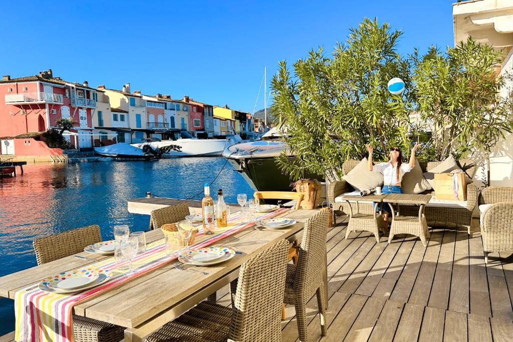 une femme assise sur une terrasse avec une table et un bateau dans l'établissement Renovated house with WIFI AC a large terrace and a mooring, à Grimaud