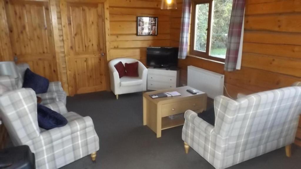 a living room with two white chairs and a tv at Hand built log cabin at Avonvale Holiday Lodges in Evesham