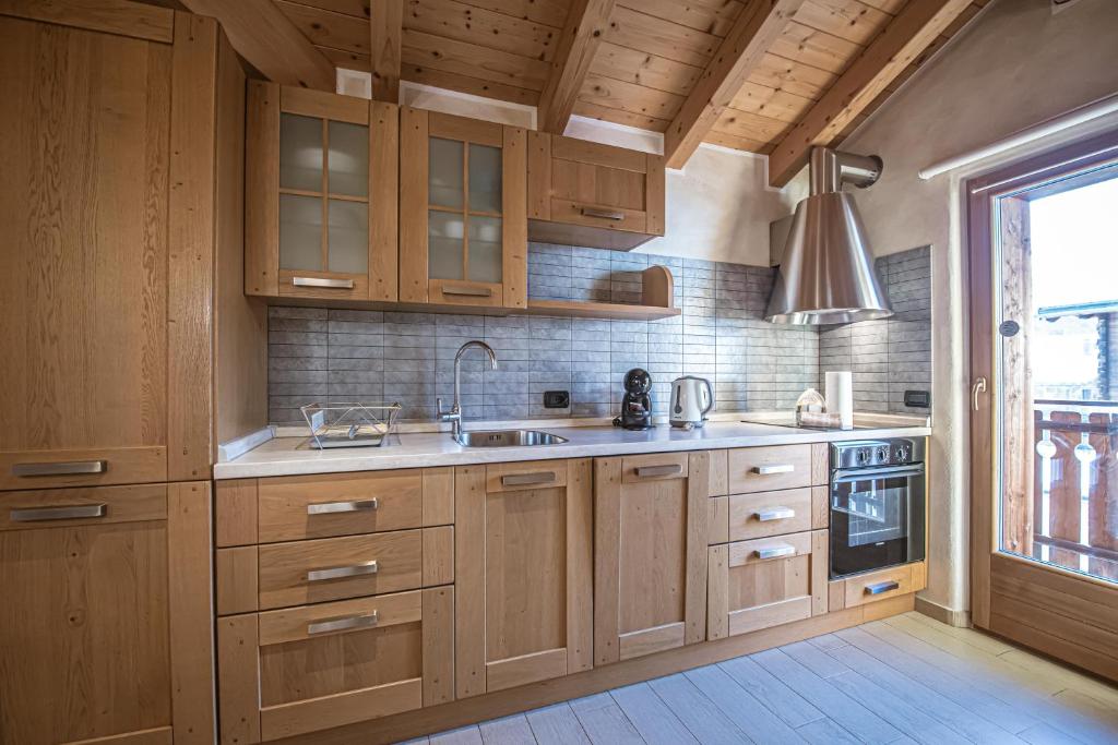 kuchnia z drewnianymi szafkami, umywalką i oknem w obiekcie Apartments & Rooms MyHolidayLivigno w Livigno