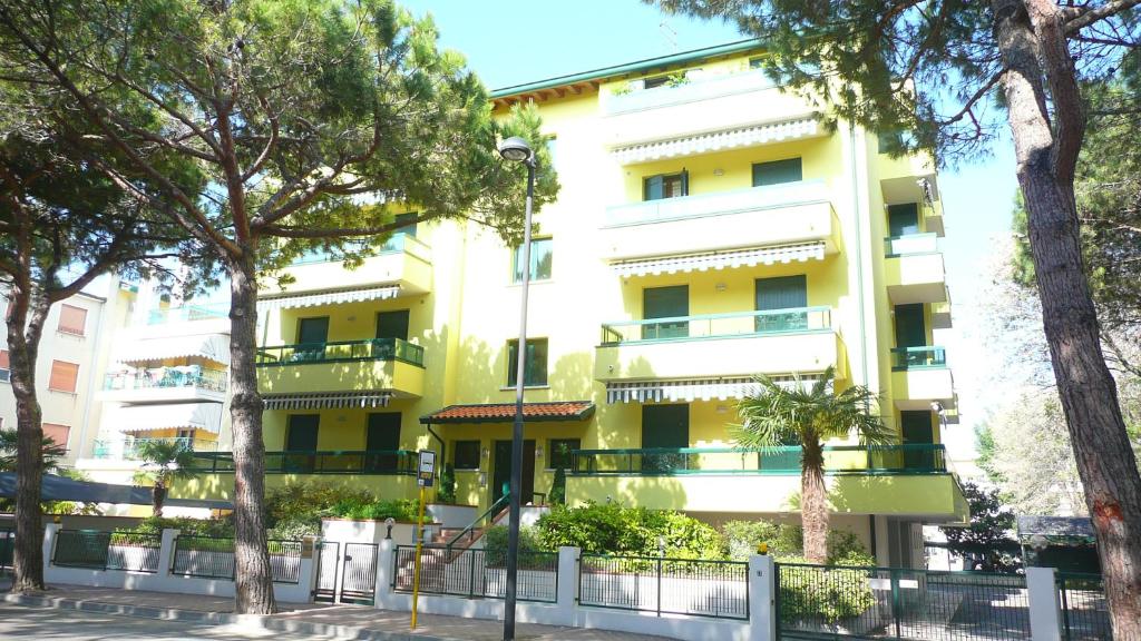 un edificio amarillo con árboles delante de él en Residence Pineta - Agenzia Cocal, en Caorle