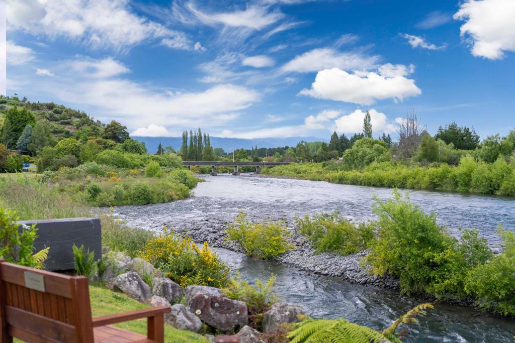 a bench next to a river with a bridge in the background at Tongariro Base Camp - Turangi Holiday Home in Turangi