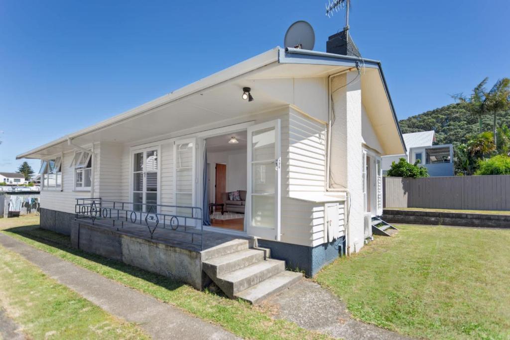 a small white house with a porch and stairs at Downtown Cosy Cottage in Mount Maunganui