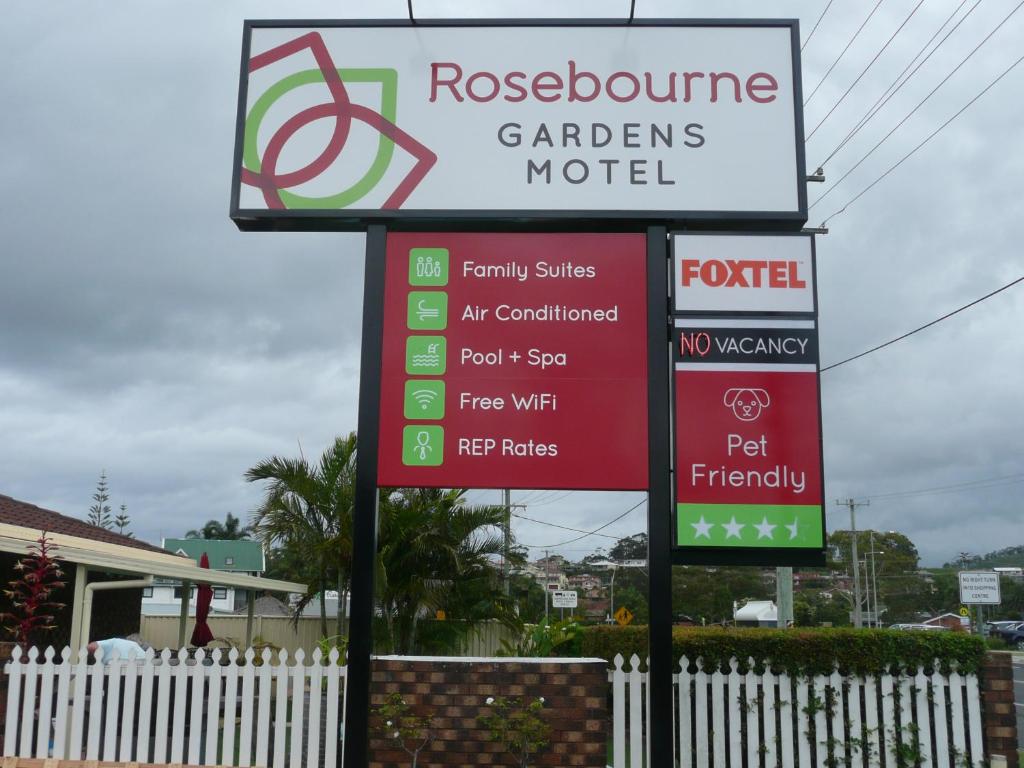 a sign for a car dealers motel next to a fence at Rosebourne Gardens Motel in Woolgoolga