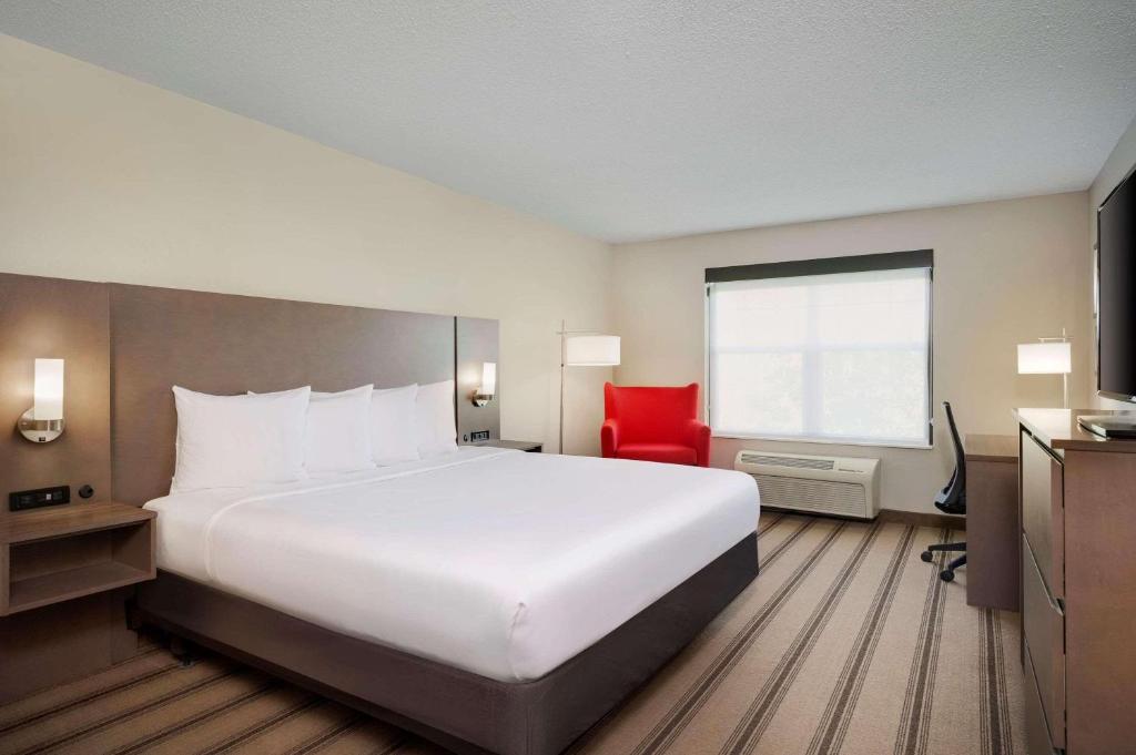 アルバートビルにあるCountry Inn & Suites by Radisson Albertville near Outlet Mallの白い大型ベッドと赤い椅子が備わるホテルルームです。