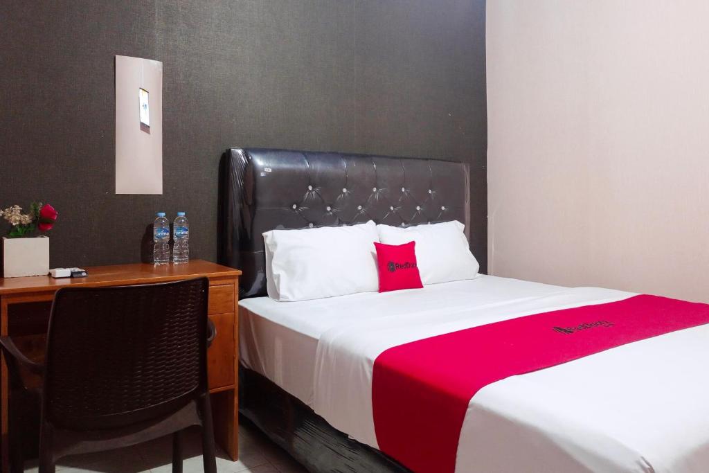 a bedroom with a bed and a desk with a red blanket at RedDoorz at Hotel Island Bengkulu in Bengkulu