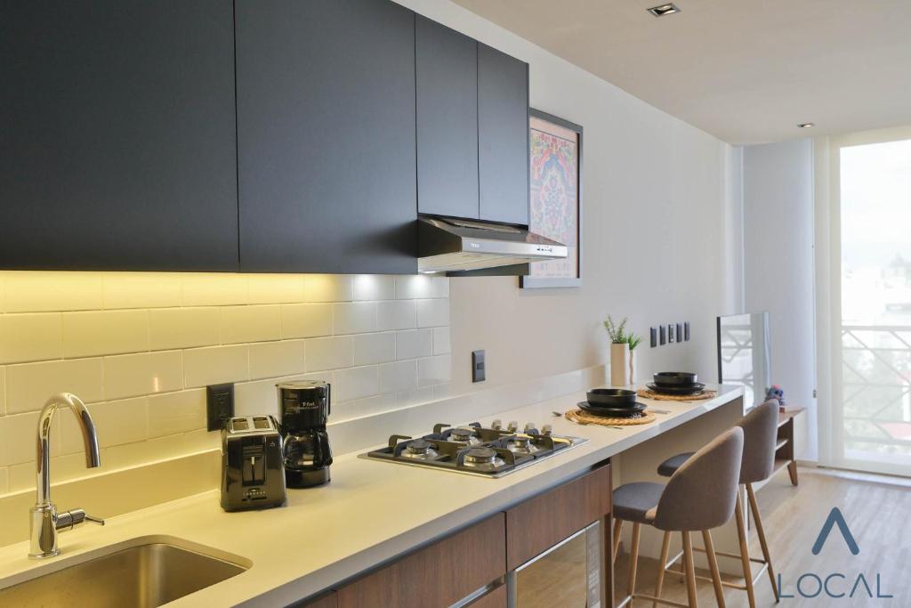 A compact apartment kitchen with a sink, gas cooktop, coffee equipment and counter seating.