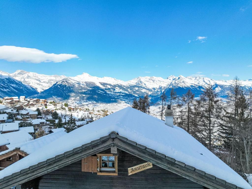 um telhado coberto de neve de um edifício com montanhas ao fundo em Chalet Anusach by Interhome em Nendaz