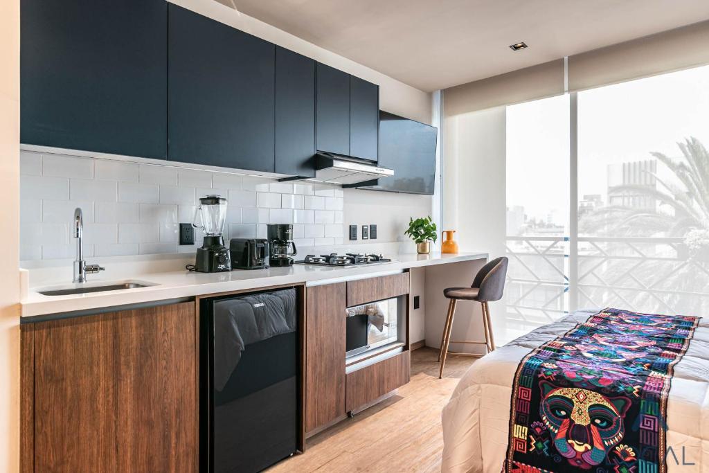 A compact studio combining a full kitchen, work perch and bed beside large windows.